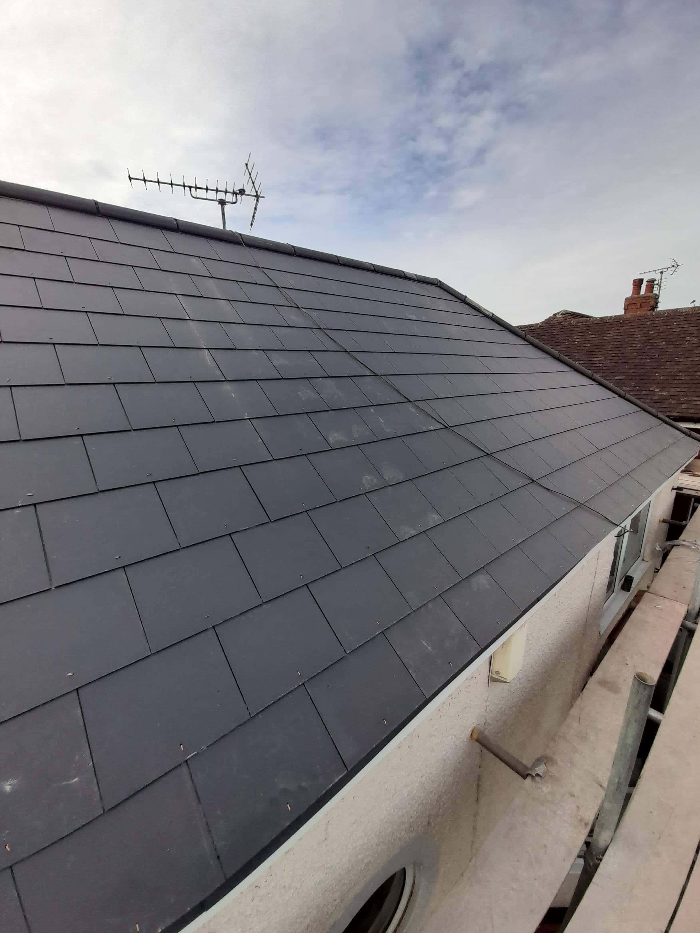Newly completed pitched roof with dark grey slate tiles and TV aerial