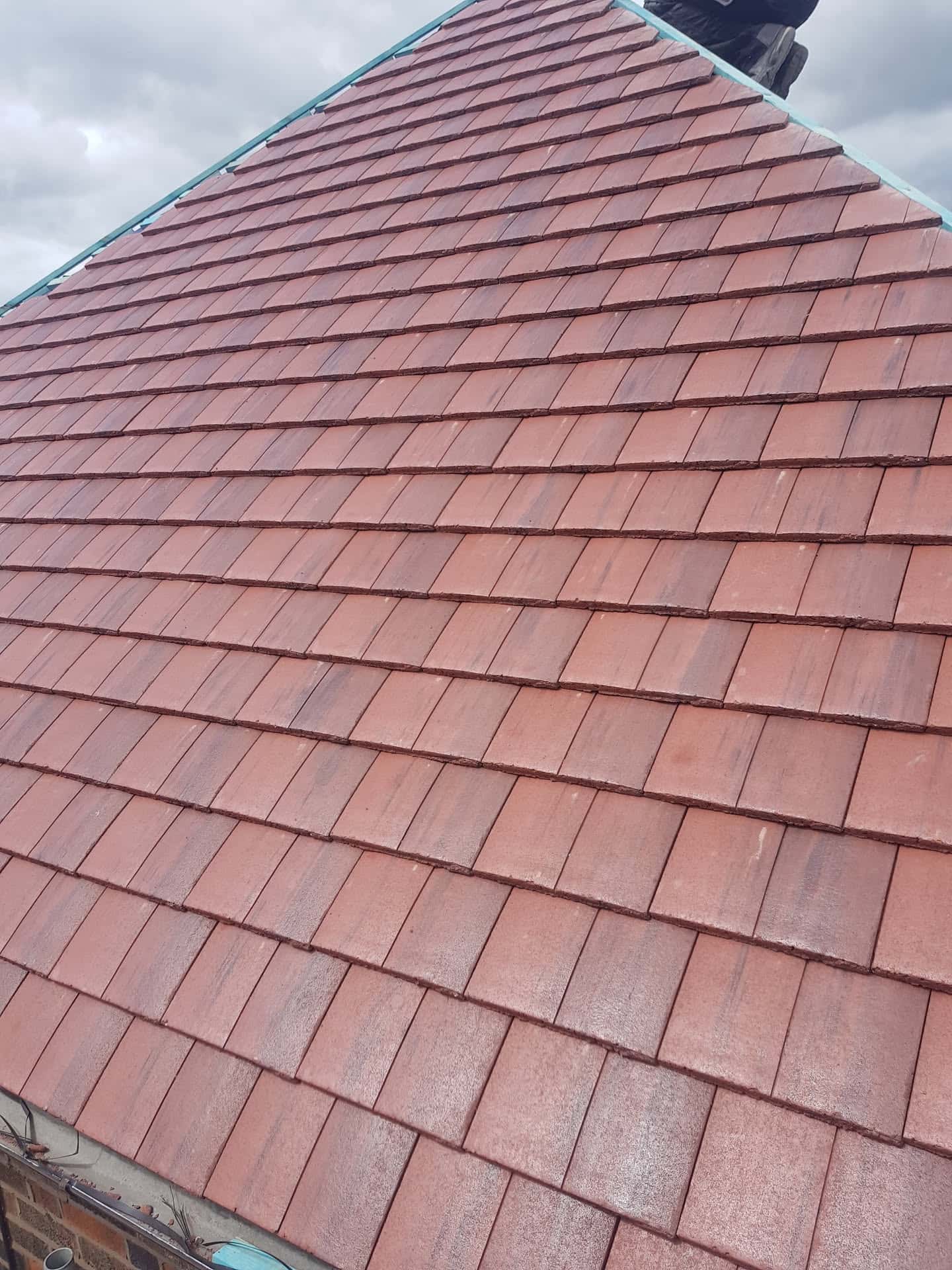 Newly completed pitched roof with red clay tiles and ridge, fitter visible at apex