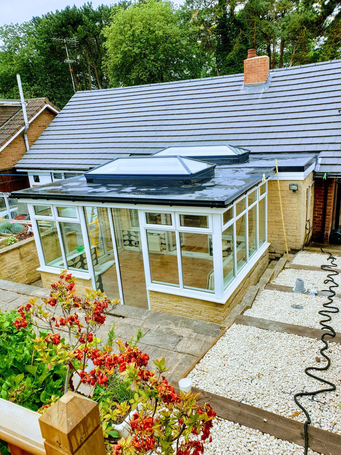 Newly installed grey tiled pitched roof with brick chimney and flat-roofed conservatory extension with skylights
