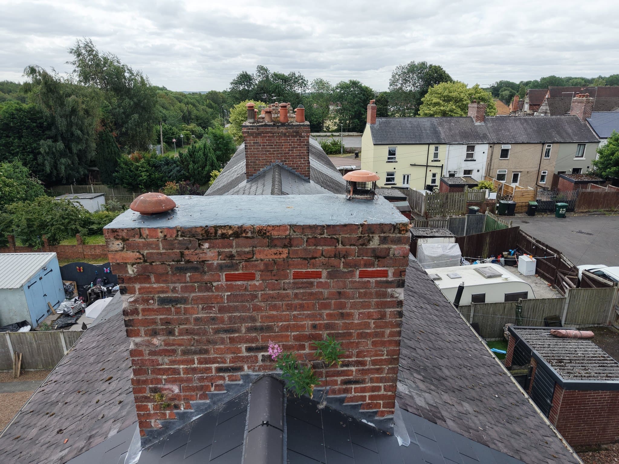 Drone survey photo of a weathered brick chimney stack with eroded mortar joints and a weed growing from the brickwork at ridge height