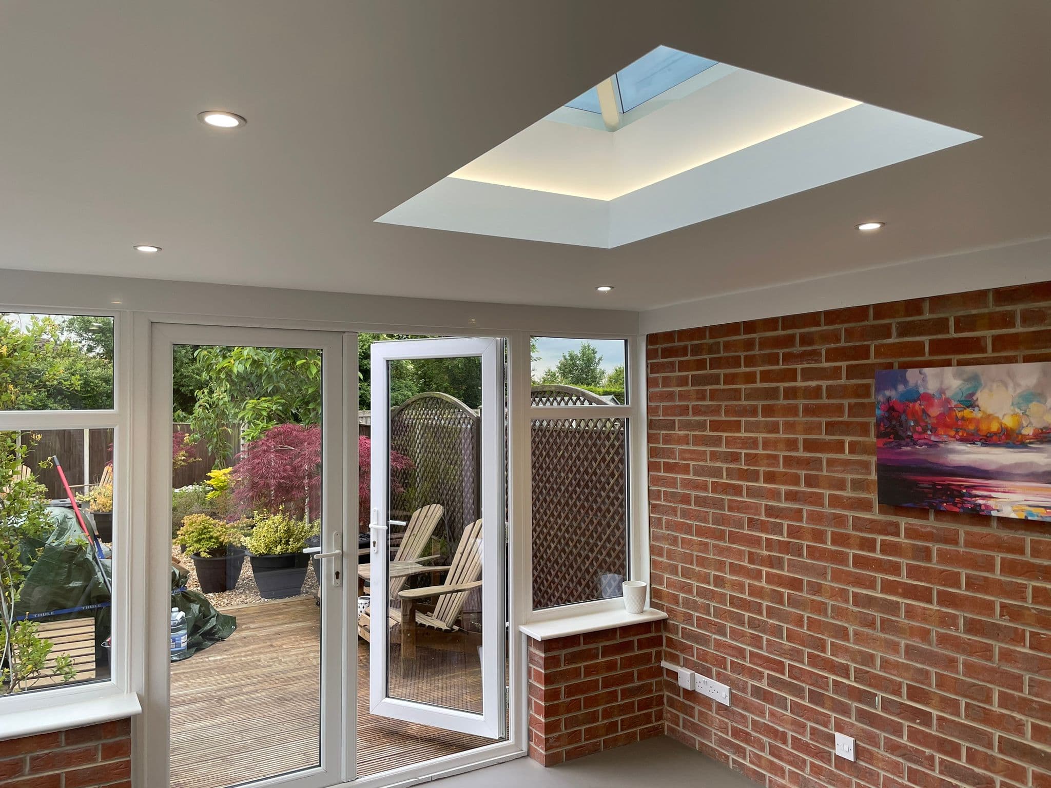 Inside the conservatory — flat plastered ceiling with a glowing central skylight and recessed downlights